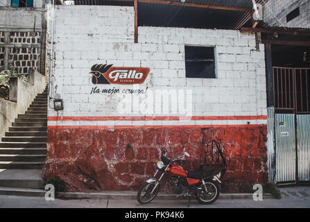 Rote Motorrad vor einer Bar mit Logo von Gallo, Guatemala nationalen Bier, spraypainted auf der Wand geparkt Stockfoto