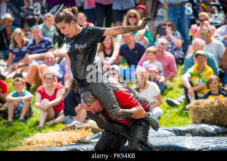 Mann, der eine Frau über eine schmutzige und nasse Hindernisparcours im Tiefland Spiele in Thorney, Somerset, England Stockfoto