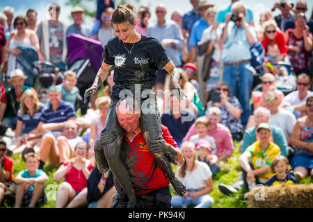 Mann, der eine Frau über eine schmutzige und nasse Hindernisparcours im Tiefland Spiele in Thorney, Somerset, England Stockfoto