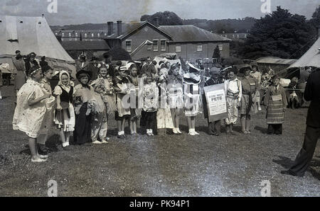 1950, historische, in einem nach dem Zweiten Weltkrieg Deutsch Sommer fete an der Kapelle Feldern, in der Nähe von East Grinstead, junge Kandidaten der childrens Fancy Dress Wettbewerb Line-up in einem Feld außerhalb ihrer Kostüme, England, UK zu zeigen. Kostüme auf Anzeige gehören 'Little bo-peep", ein Teehaus Kellnerin, und Metzger, mit einem Schild, auf dem "eine Gemeinsame der Rationen!'. Stockfoto