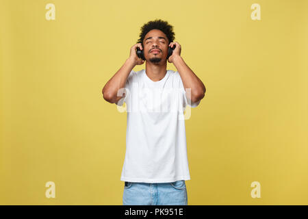 Close up Portrait von dunkelhäutigen Mann mit geschlossenen Augen, Kopfhörer, hört Musik. Teenager genießt Audiospur auf gelbem Hintergrund. Stockfoto