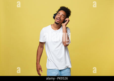 Close up Portrait von dunkelhäutigen Mann mit geschlossenen Augen, Kopfhörer, hört Musik. Teenager genießt Audiospur auf gelbem Hintergrund. Stockfoto