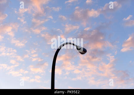 Gebogene streetlight gegen den blauen Himmel Silhouette mit puffy Rosa altocumulus Wolken bei Sonnenuntergang Stockfoto