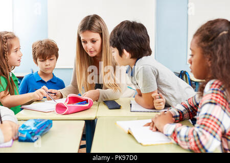 Frau als Lehrerin hilft bei den Hausaufgaben oder gibt Nachhilfe in der Grundschule Stockfoto