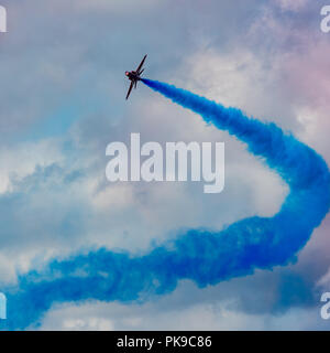 Eine dicke Rauchwolke blauer Rauch aus einem Red Arrows Hawk Jets vermischt sich mit rosa gefärbten Wolken Stockfoto