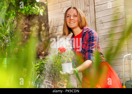 Frau Bewässerung Garten Blumen mit Schlauch Sprinkler Stockfoto