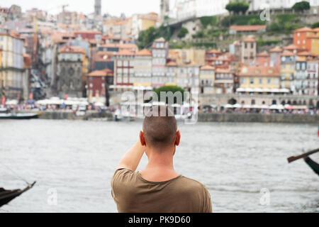 Nahaufnahme eines jungen kaukasischen Mann, von hinten gesehen, ein Bild von den Fluss Douro und Porto, Portugal, mit seinem Smartphone, von Vila Nova de Stockfoto