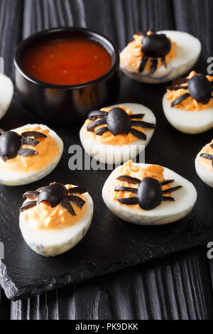 Halloween Menü Russische Eier mit Senf gefüllt und mit Olivenöl Spinnen in der Nähe eingerichtet - bis auf einen Schwarzen Tisch. Vertikale Stockfoto