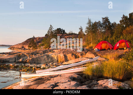 Ein Mann am Camp und Kajaks, wie die Abendsonne taucht die Felsen in goldenes Licht. Stockfoto