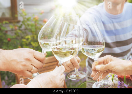 Familie unterschiedlichen Alters Menschen fröhlich feiern im Freien mit Gläsern Weißwein, verkünden Toast Menschen mit Abendessen in einem Haus Garten im Sommer Sonnenlicht. Stockfoto