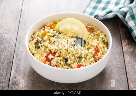 Couscous mit Gemüse in Schale auf Holztisch. Stockfoto