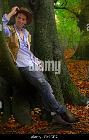 Ein Mann gekleidet wie ein Cowboy gegen einen Baumstamm lehnt. Stockfoto