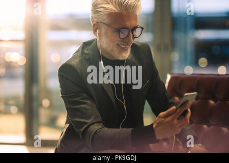 Reifen Geschäftsmann in Office Lobby die Videokonferenz mit seinem Smart Phone sitzen. Kaukasische Mann mit weissen Haaren in Büro und Videokonferenz. Stockfoto