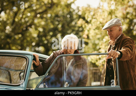 Alten weißen Mann, ein Gentleman und Öffnen der Autotür für sein Datum. Frau ins Auto mit Mann öffnete die Tür von der winterlichen Tag. Stockfoto