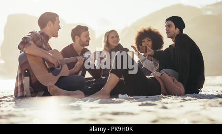 Junger Mann mit Gitarre für Freunde am Strand. Eine Gruppe von Freunden, die Party am Meer.