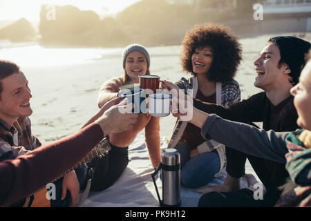Gruppe von multi-ethnischen Jugendliche toasten Kaffeetassen am Strand. Eine Gruppe von Freunden die Zeit zusammen am Strand/in. Stockfoto