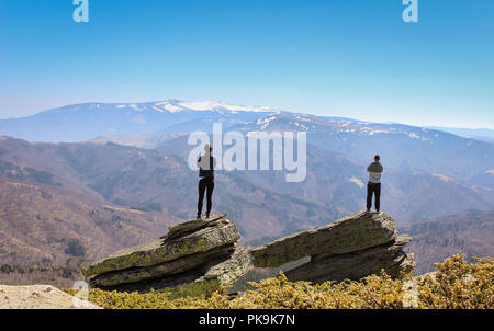 Junges Paar von zwei großen Felsen auf dem Gipfel und auf der Suche an einem entfernten Berge Stockfoto