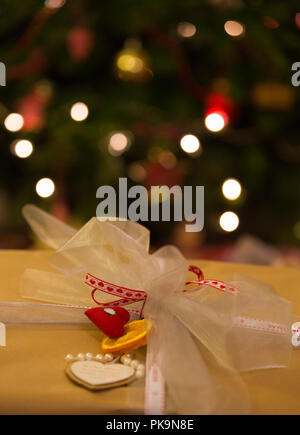 Wickelte Weihnachtsgeschenk, unscharf Weihnachtsbaum mit Lichterkette im Hintergrund Stockfoto
