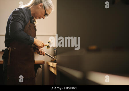 Ältere Frau, die mit traditionellen Tools in Ihre Werkstatt Schmuck. Frau Goldsmith aus Leder Schürze und Gläser, einen Ring an einer Werkbank u Stockfoto