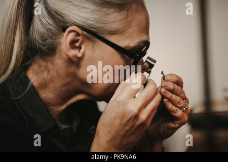 Nahaufnahme von Frau Juwelier diamant Prüfung Lupen-funktion Werkstattarbeit. close-up Senior weiblichen Juwelier bei Diamond durch Lupe Lupe suchen. Stockfoto