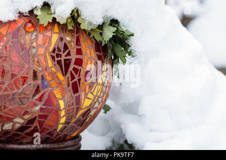 Kalten Schnee Tag mit close-up von Gold, Rot, Gelb, Orange, Leuchtend bunte Glasfenster Mosaik Garten kunst Ball im Winter und grüne Blätter Stockfoto