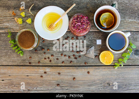 Tee, Kaffee in Tassen, Chicorée, Zitrone, Minze, Marmelade aus Rosenblättern, getrockneter Kalk, Honig auf dem alten Holz- Hintergrund. Getönten Bild. Ansicht von oben. Stockfoto