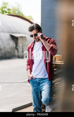 Vorderansicht des Jungen stilvollen Mann stand in der Nähe von Holzpaletten und Sonnenbrille einstellen Stockfoto
