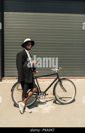 Stilvolle Mann mit weißem T-Shirt und Jacke mit Smartphone, während sein Fahrrad Holding Stockfoto