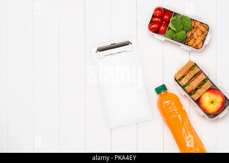 Gesundes Mittagessen Boxen mit Sandwich, frisches Gemüse, Obst und Nüsse auf weißem Holz- Hintergrund. Von oben gesehen Stockfoto