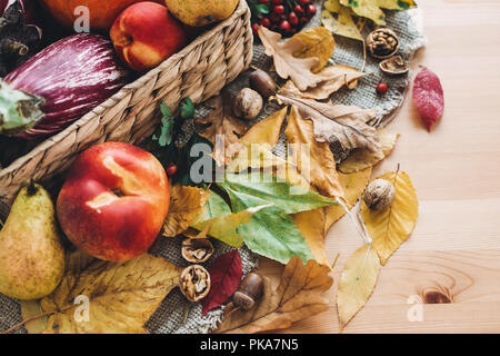 Schönen Herbst Kürbis und Gemüse in den Korb und bunte Blätter mit Eicheln und Nüsse auf Holztisch, Ansicht von oben. Herbst helles Bild. Die Zeit der Ernte. Stockfoto