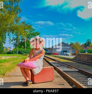 Adorable kleine Mädchen auf einem Bahnhof und warten auf den Zug mit Vintage Koffer. Reisen, Urlaub und chilhood Konzept. Reiseversicherung conc Stockfoto