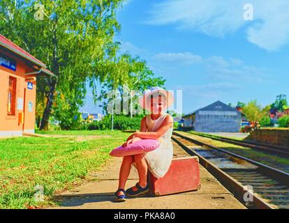 Adorable kleine Mädchen auf einem Bahnhof und warten auf den Zug mit Vintage Koffer. Reisen, Urlaub und chilhood Konzept. Reiseversicherung conc Stockfoto