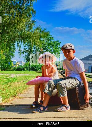 Adorable kleinen Mädchen und Jungen auf einem Bahnhof und warten auf den Zug mit Vintage Koffer. Reisen, Urlaub und chilhood Konzept. Reise Versicherung Stockfoto