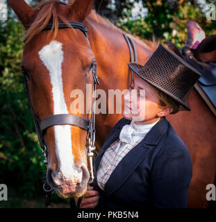 Eine elegante junge Frau mit ihrem Pferd in traditionellen reiten Top Hat und Gesichtsschleier gekleidet Stand Stockfoto