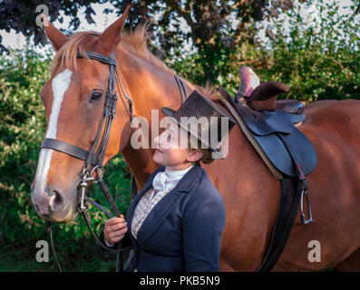 Eine elegante junge Frau mit ihrem Pferd in traditionellen reiten Top Hat und Gesichtsschleier gekleidet Stand Stockfoto