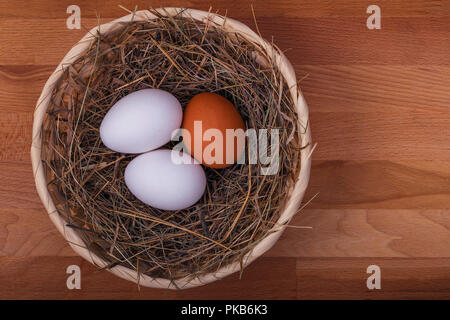 Drei Huhn Eier in einem Korb mit Stroh auf einer hölzernen Hintergrund Stockfoto