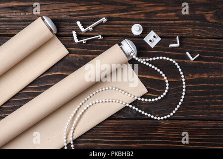 Die gerollte beige Fensterläden ist auf einem hölzernen Oberfläche. Beigefarbene Markisen liegen auf einem alten Holztisch. Stockfoto