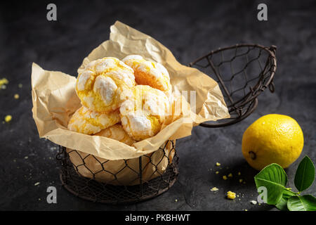 Hausgemachte Zitrone crinkle Plätzchen mit Puderzucker Puderzucker auf Trägerpapier in kleinen Metall, auf dunklem Hintergrund Stockfoto