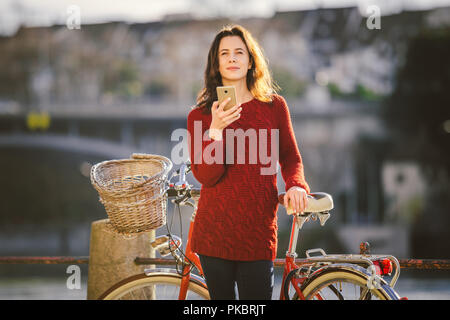 Thema Tourismus auf dem Fahrrad und moderner Technologie. Schönen jungen kaukasischen Frau steht in der Nähe von red retro Fahrrad auf Riverside Rhein Basel Schweizer gewinnen Stockfoto