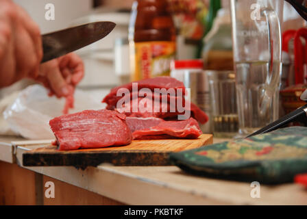 Metzger mann Schneiden von Fleisch auf dem Holzbrett in der Küche. Lebensstil Stockfoto