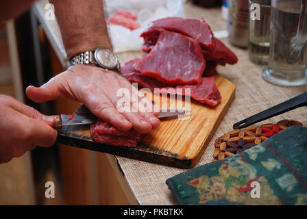 Metzger mann Schneiden von Fleisch auf dem Holzbrett in der Küche. Lebensstil Stockfoto