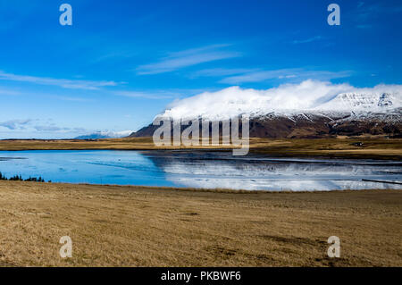 Schnee und bedeckte cloud Berge neben Wiesen und das Meer bei Leiruvogur Cove, Island Stockfoto