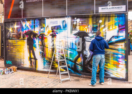 Ein Graffiti Künstler erstellen einer bunten regnerischen Nacht Zeit Straßenszene in Spitalfields, London, England, Großbritannien Stockfoto