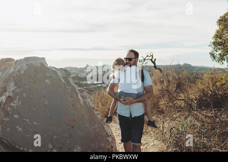 Ein Vater trägt seine junge Tochter auf einem Wanderweg; Los Angeles, Kalifornien, Vereinigte Staaten von Amerika Stockfoto