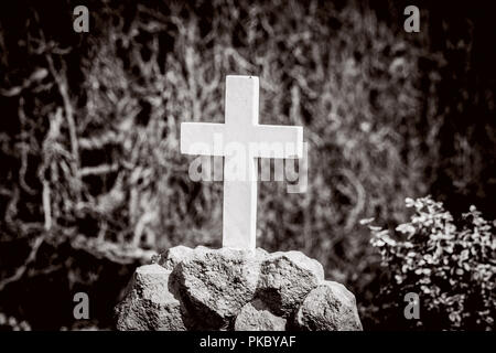 Weißes Kreuz auf einem Grab in Sepia Farben auf einem Friedhof Stockfoto