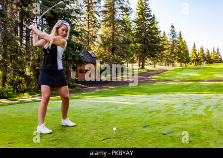 Ein weiblicher Golfspieler an der Oberseite ihrer Schwingen, als sie sich bereit, den Ball zu schlagen nach dem Einrichten Ihrer geschossen; Edmonton, Alberta, Kanada Stockfoto