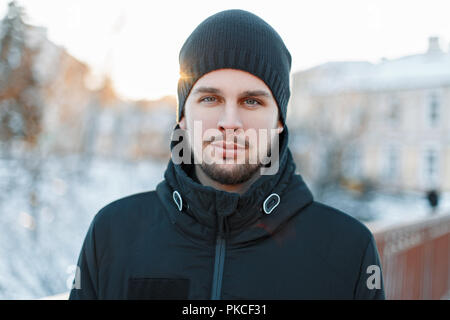 Schönen winter Portrait von einem gutaussehenden Mann in einem strickmütze bei Sonnenuntergang Stockfoto