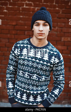 Junge stilvolle Hipster in einem Strick Pullover mit Mustern und ein Hut auf einem Hintergrund von Red brick wall Stockfoto