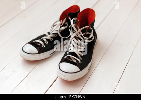 Alte schwarze Turnschuhe mit Rot auf Holz- Hintergrund Stockfoto