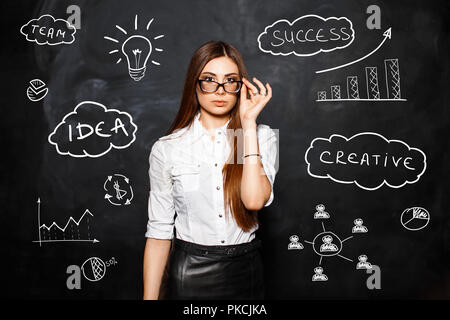 Die junge schöne Mädchen mit Brille in einer weißen Bluse auf dem Hintergrund der Symbole und Diagramme. Das Konzept einer erfolgreichen Geschäftsfrau Stockfoto